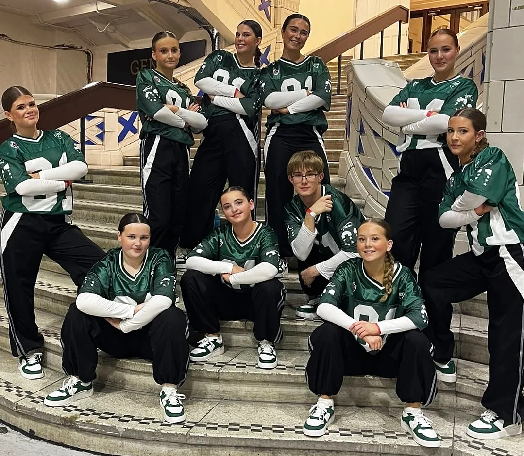Street dance team in green jerseys and black tracksuit bottoms posing on a staircase